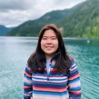 Aina Hori in front of water and green mountains