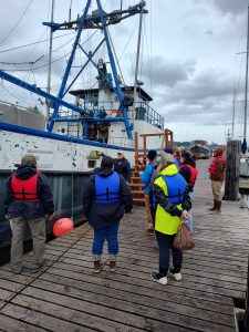 Skills and Drills students stand with instructor Robert Maw on a dock in front of a practice vessel.