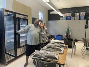 Maggie Michaels and Patrick McKnight in front of a freezer. A table in front of them holds butchered fish.