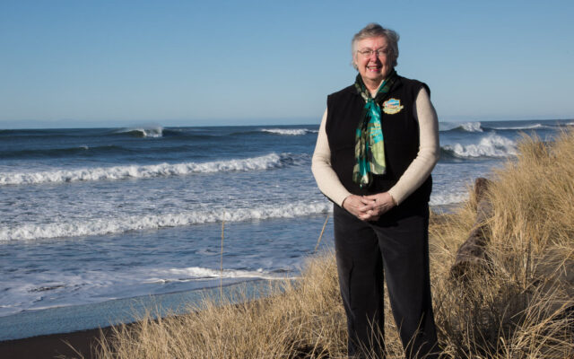 Crystal Dingler stands on a beach in front of ocean waves.
