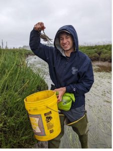 Zach Levitan with a yellow bucket holding up a green crab