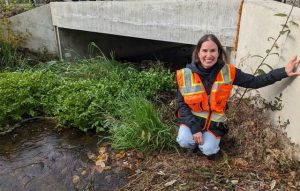 Sunny Jardine kneels next to a culvert
