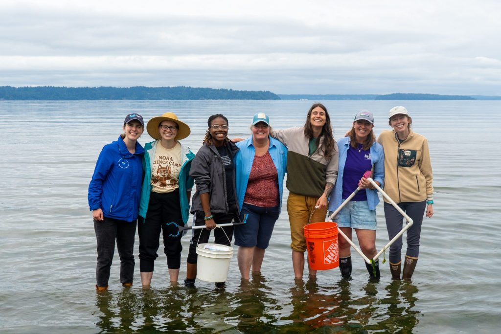 NOAA experts and volunteers stand in a line, ankle-deep in water.