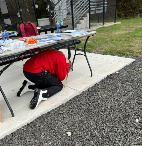 Maddie Lucas braces under a table during the Great ShakeOut drill