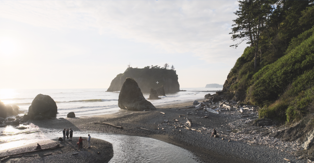 Several people standing on Ruby Beach as the sun sets over the water
