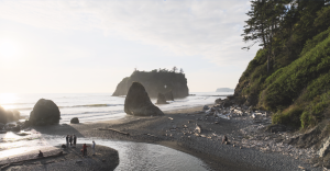 Several people standing on Ruby Beach as the sun sets over the water