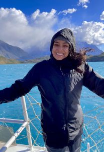 Mariah Ricci on a boat with blue water, mountains, and clouds behind.