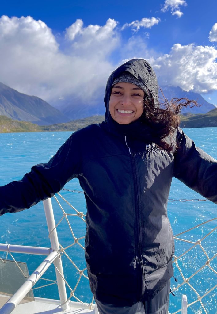 Mariah Ricci on a boat with blue water, mountains, and clouds behind.