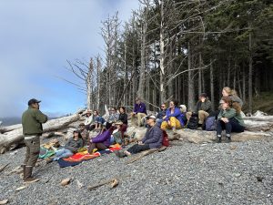 Dr. Steve Fradkin, left, addresses new fellows sitting uphill from him on a rocky beach