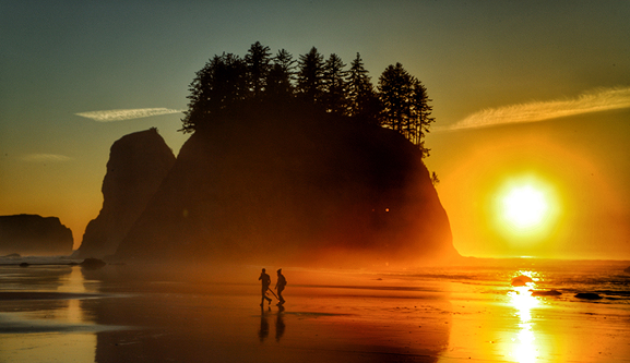 Two silhouettes of people walking on the coast