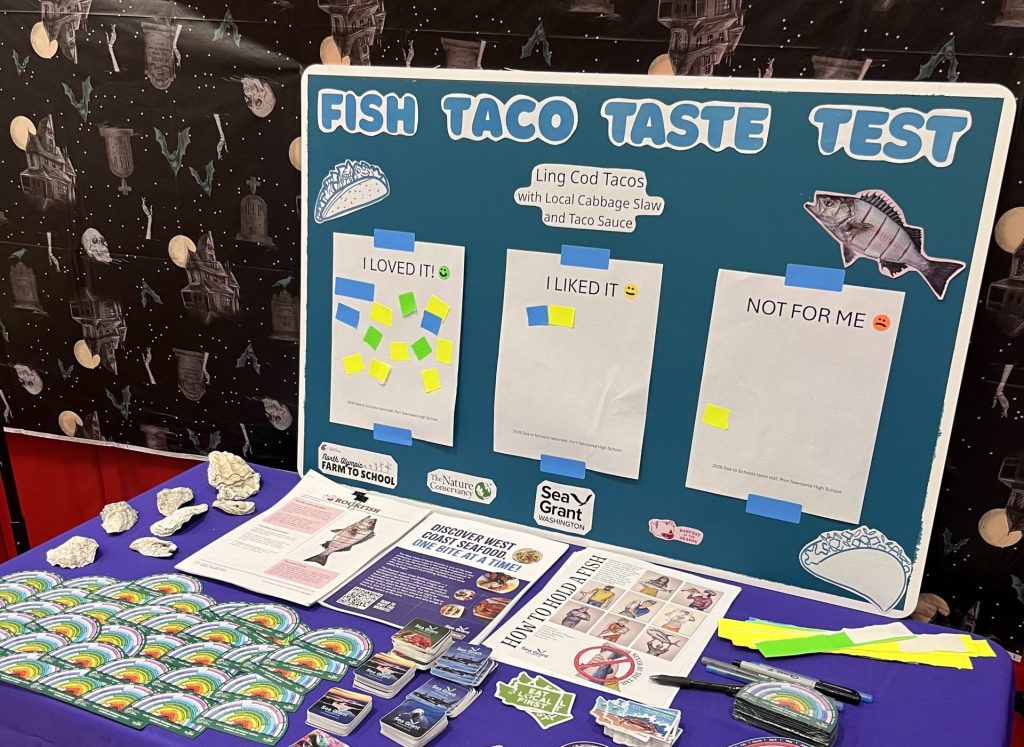 A Washington Sea Grant outreach table. A message board shows student feedback, with "loved it" having the most stickers.